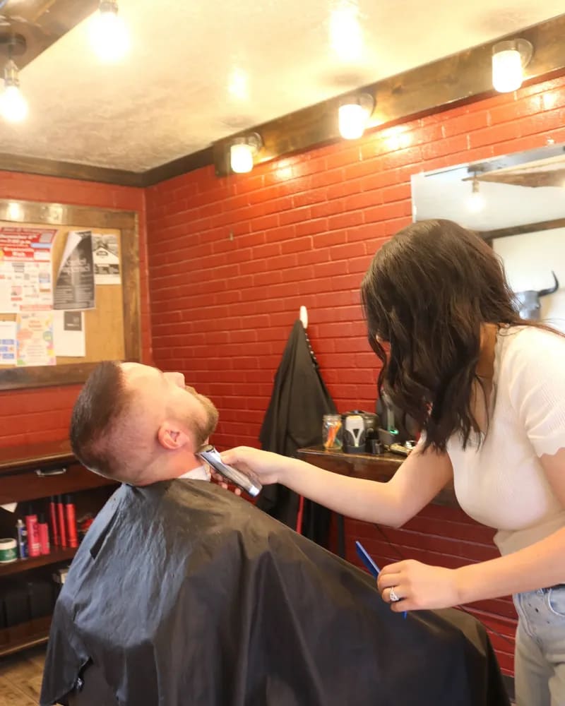 Customer reclined in the barber chair while a barber trims his beard