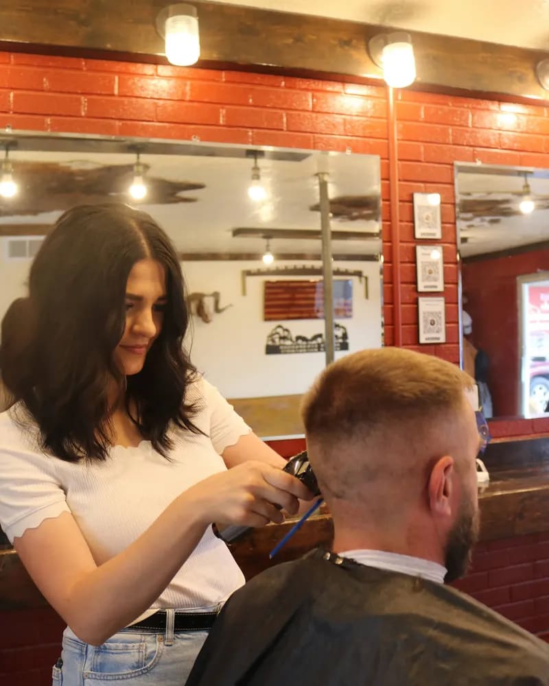 Barber cutting a short fade in front of the shop's mirrors and brick wall
