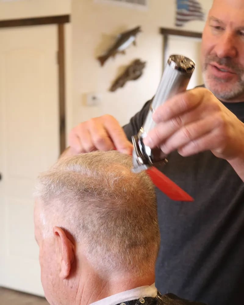 Barber trimming the back of a customer's gray hair with clippers and a red comb